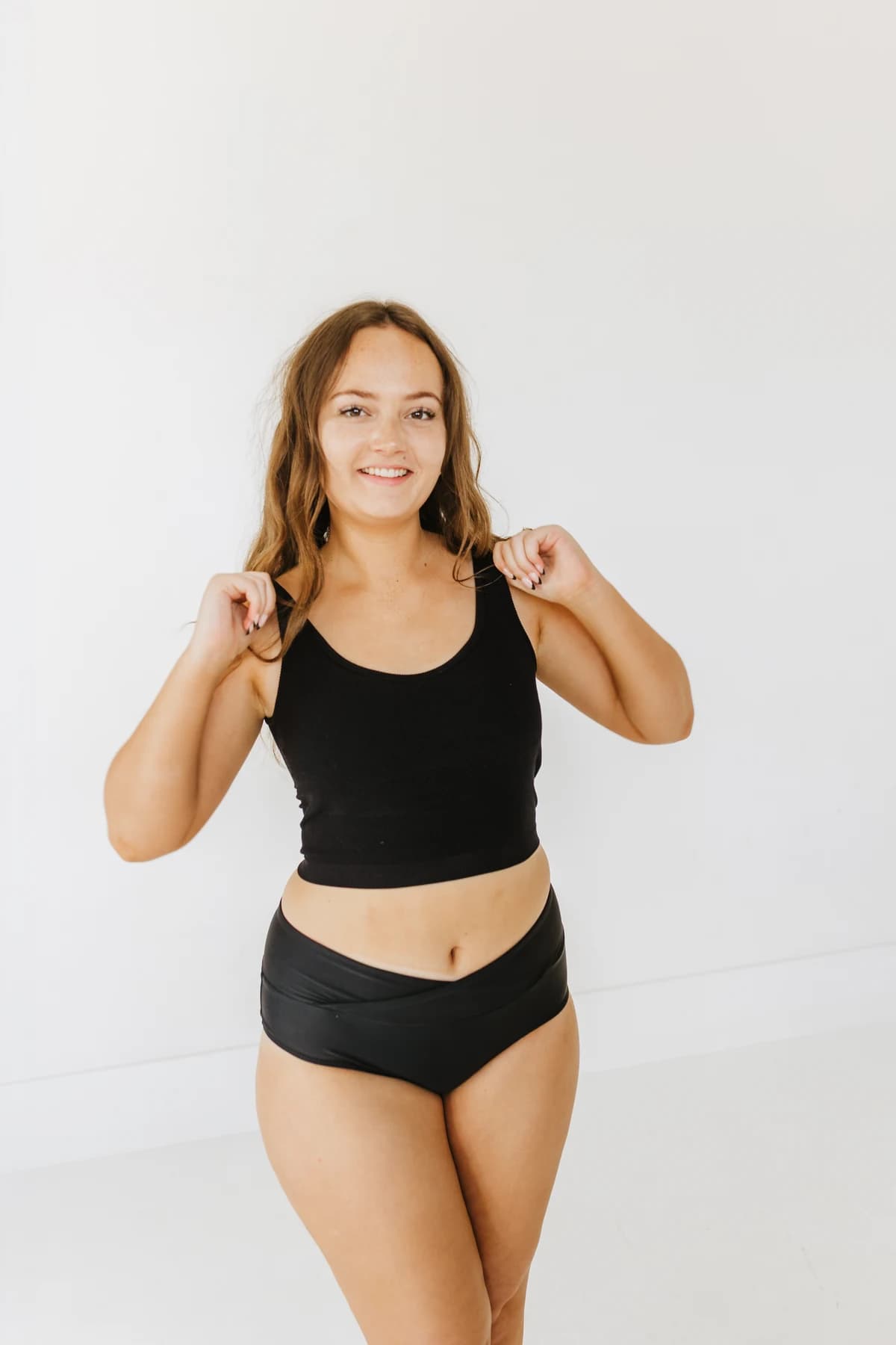 Model smiling in a black tank and swim bottoms at the SK Glow shoot
