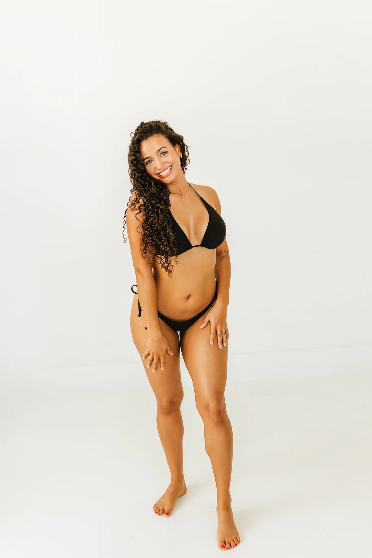 Curly-haired model posing in black swimwear at the SK Glow shoot