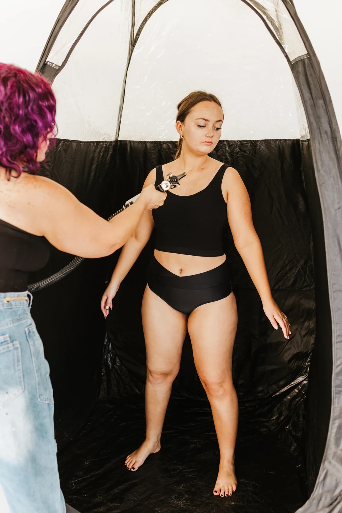 Courtney applying a custom spray tan inside a tanning tent