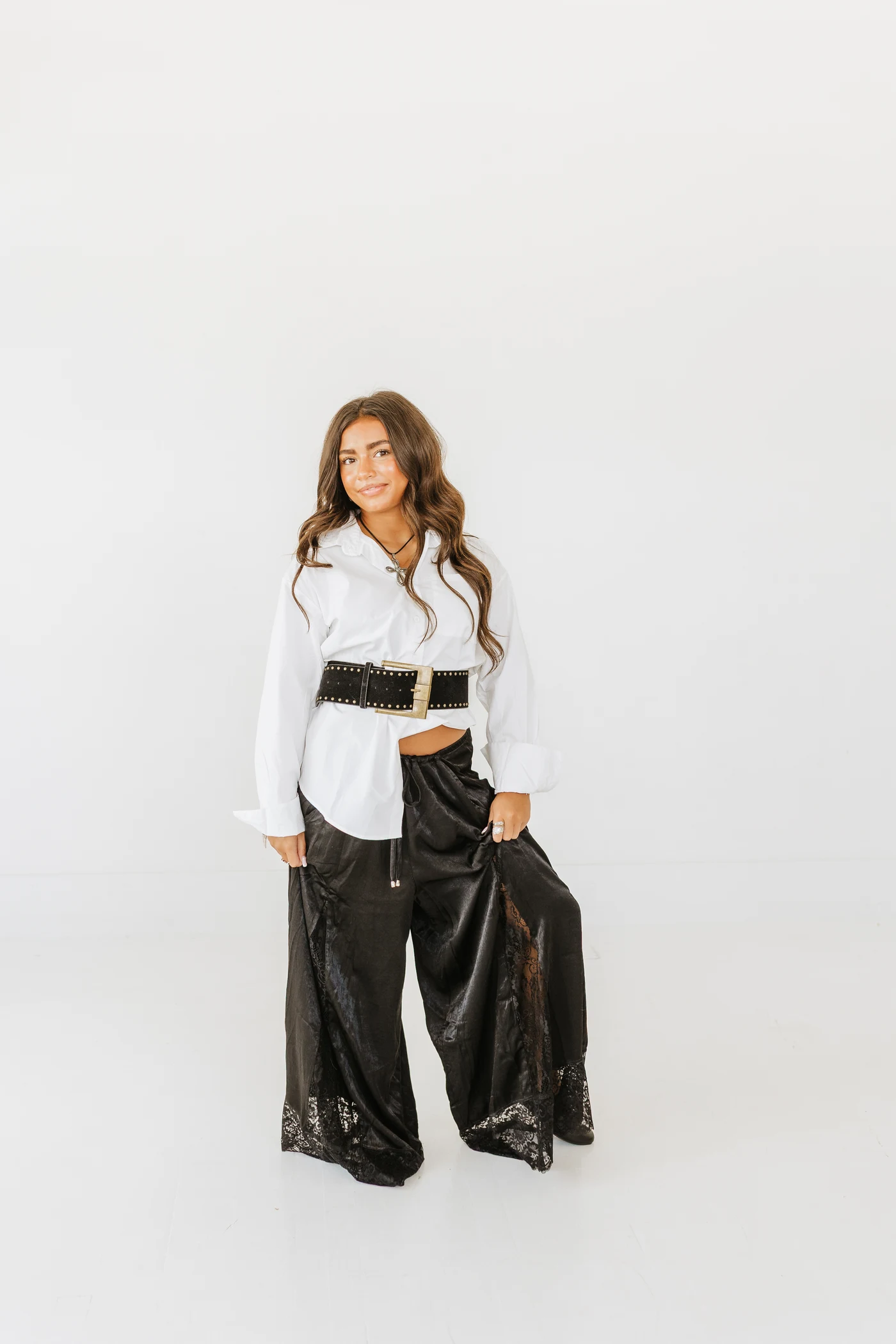 White button-down cinched with a black belt over flowing black lace-trim pants